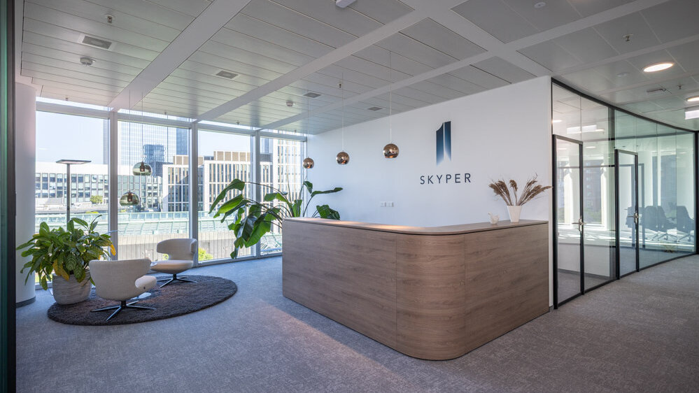 Moderner Empfangsbereich im SKYPER Frankfurt mit Rezeption, Lounge-Sesseln, Glaswänden und Blick auf die Frankfurter Innenstadt.