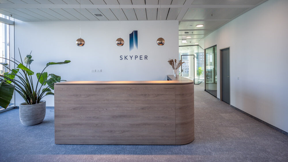 Empfang im SKYPER Frankfurt mit moderner Holzrezeption, SKYPER Logo, Pflanzen und angrenzenden verglasten Büroflächen.