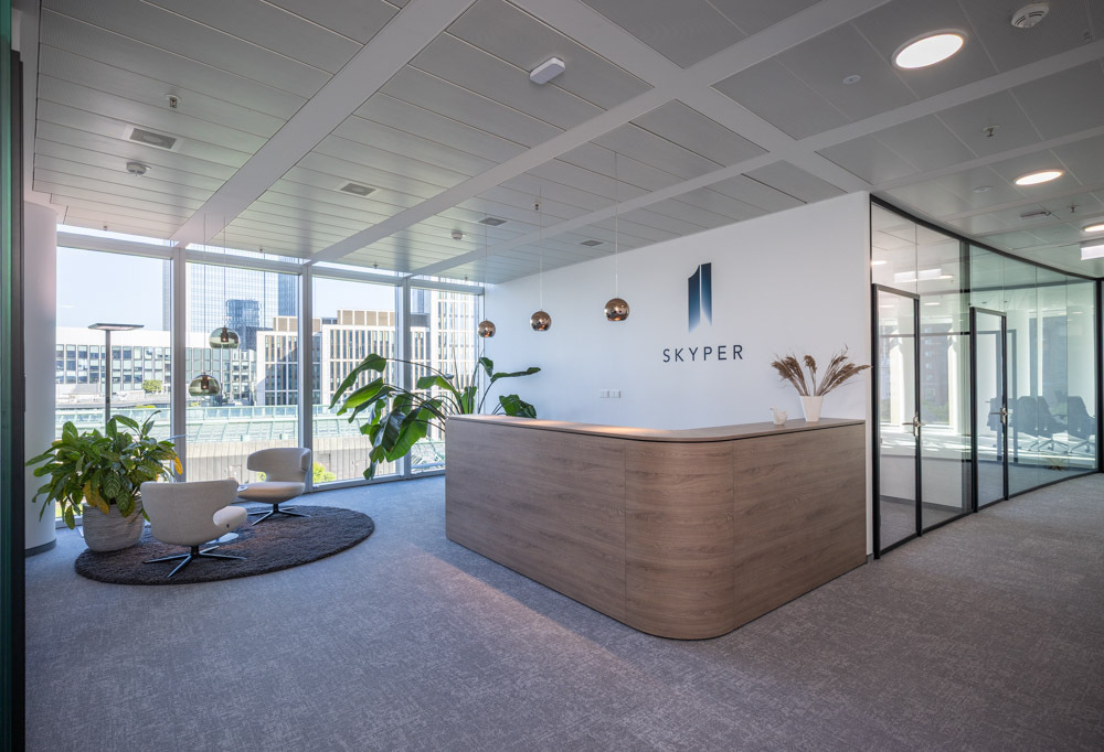 Modern reception area at SKYPER Frankfurt with front desk, lounge chairs, glass walls and views of Frankfurt city center.