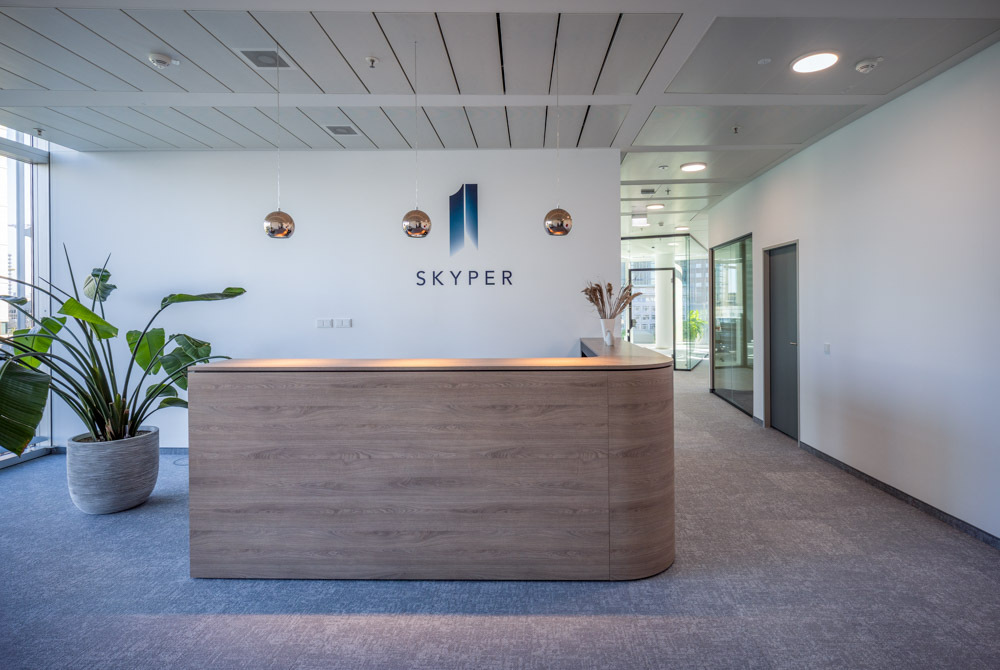 Reception area at SKYPER Frankfurt with modern wooden front desk, SKYPER logo, plants and adjacent glass office spaces.